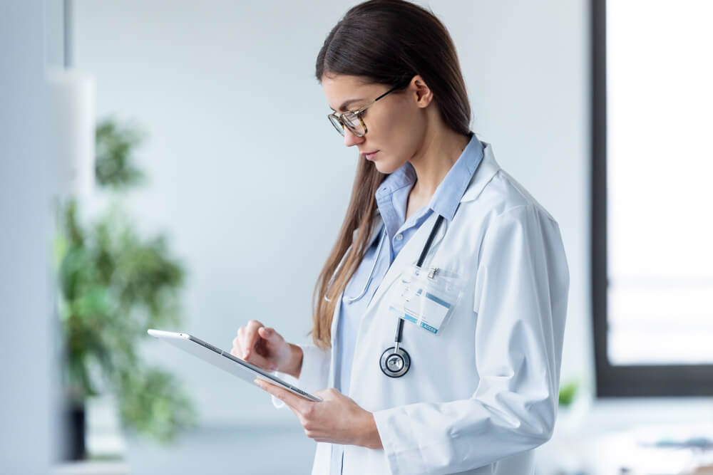 healthcare email_Shot of female doctor using her digital tablet while standing in the consultation.