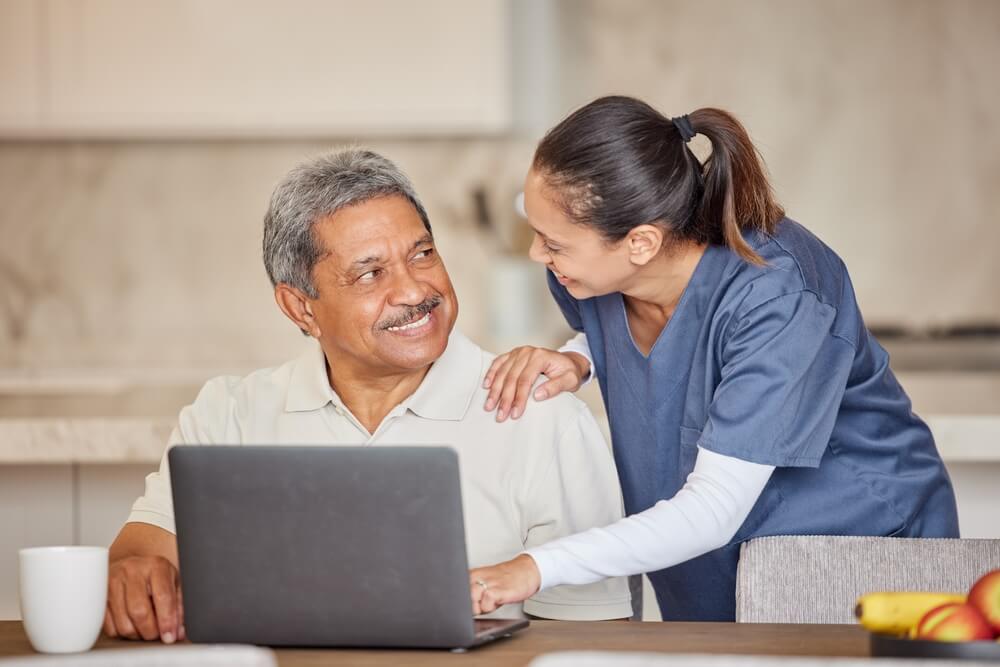 healthcare patients_Healthcare, trust and nurse help patient on laptop, reading email, good news or positive results in kitchen. Young health care worker looking happy about diagnosis, showing man how to use online app