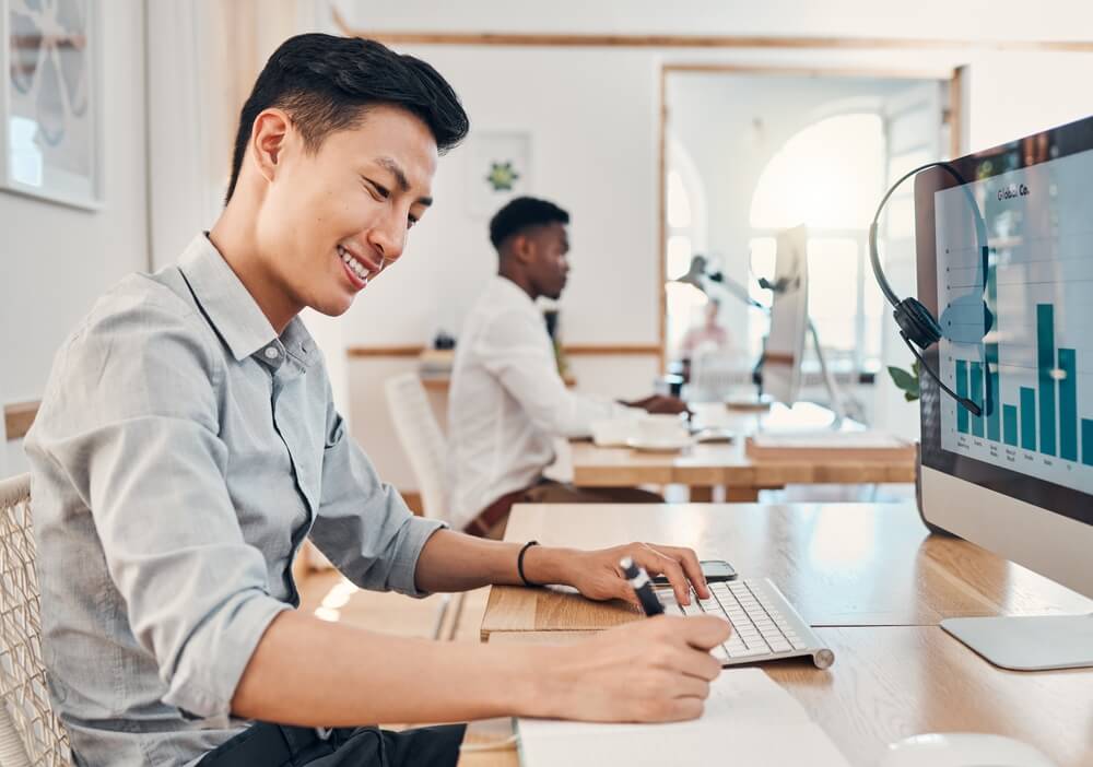 SEO Consultant_Call center, telemarketing and crm consultant writing sales report on infographics, Seo data and statistics on computer. Asian man with notebook for finance analytics, profit and performance notes