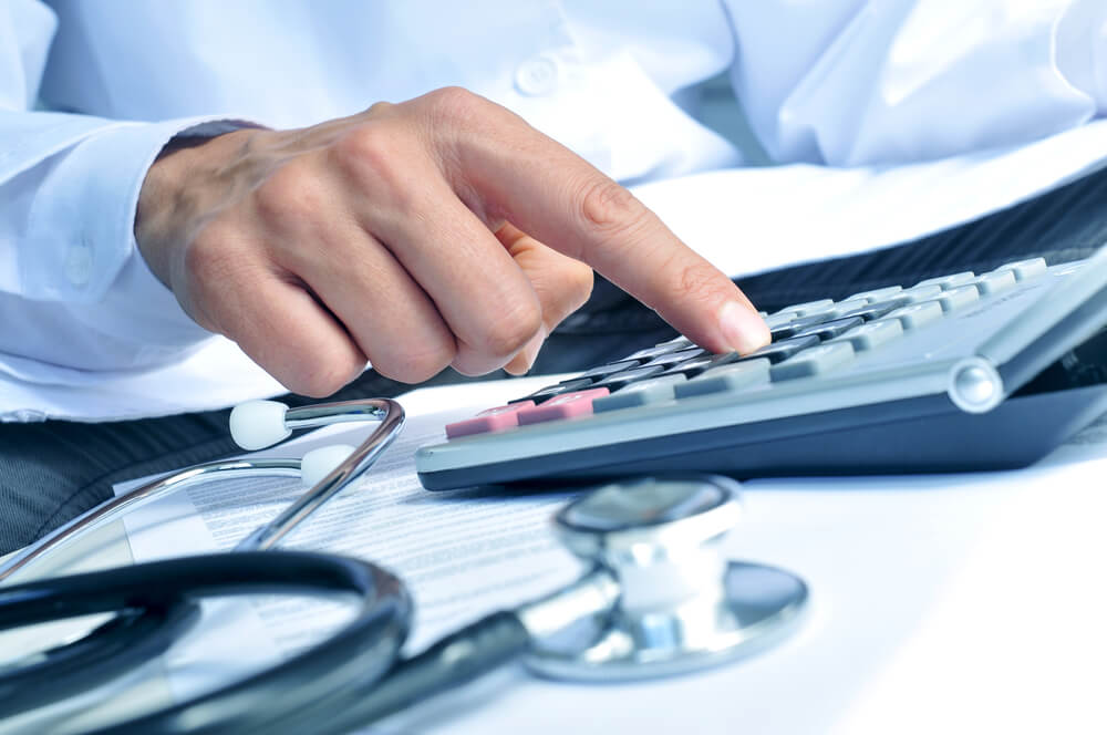 healthcare cost_closeup of a young caucasian healthcare professional wearing a white coat calculates on an electronic calculator