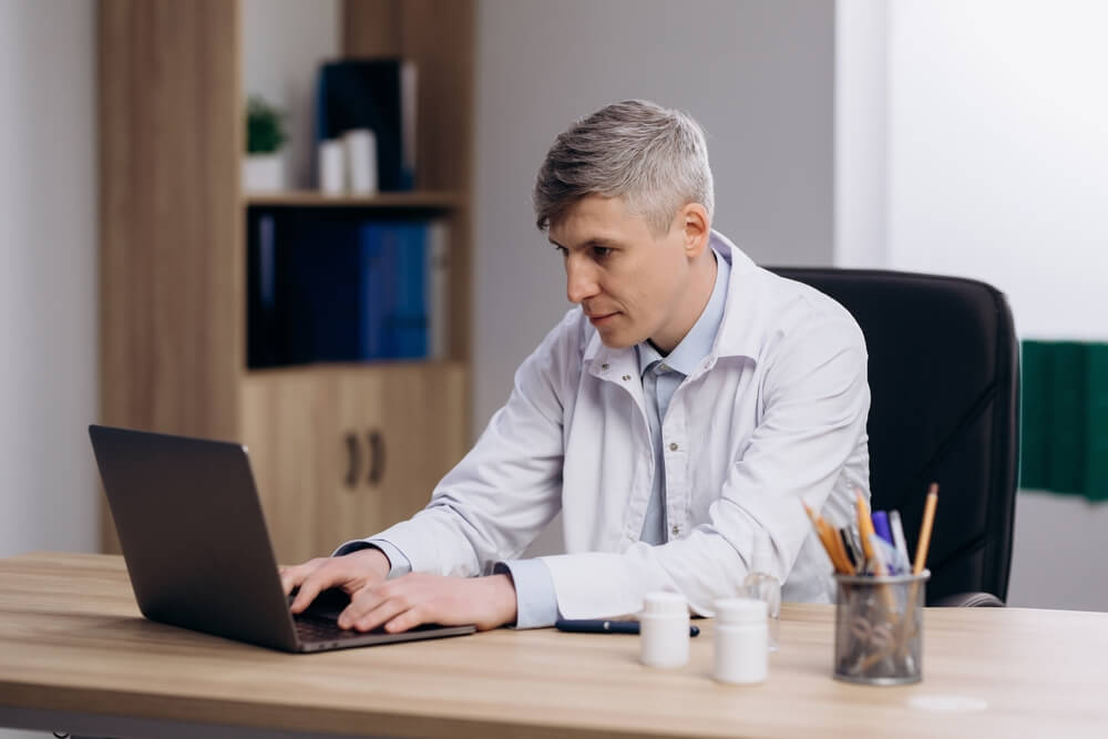 healthcare email_Male doctor in medical uniform working typing on computer. Family therapist consulting patients online through digital health platform.