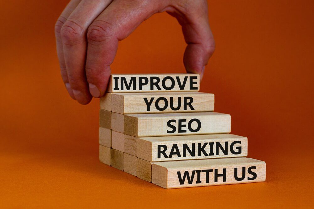 seo rank_Improve your SEO ranking with us symbol. Wooden blocks with words Improve your SEO ranking with us. Businessman hand. Beautiful orange background, copy space. Business, improve SEO ranking concept.