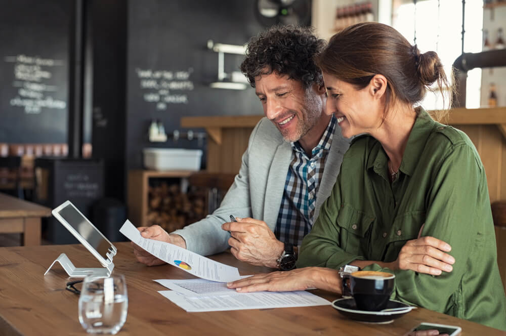 small business graphs_Portrait of mature business man and casual businesswoman sitting in cafe and discussing sales graph. Group of two middle aged coworkers working comparing forecasting graphics. Happy