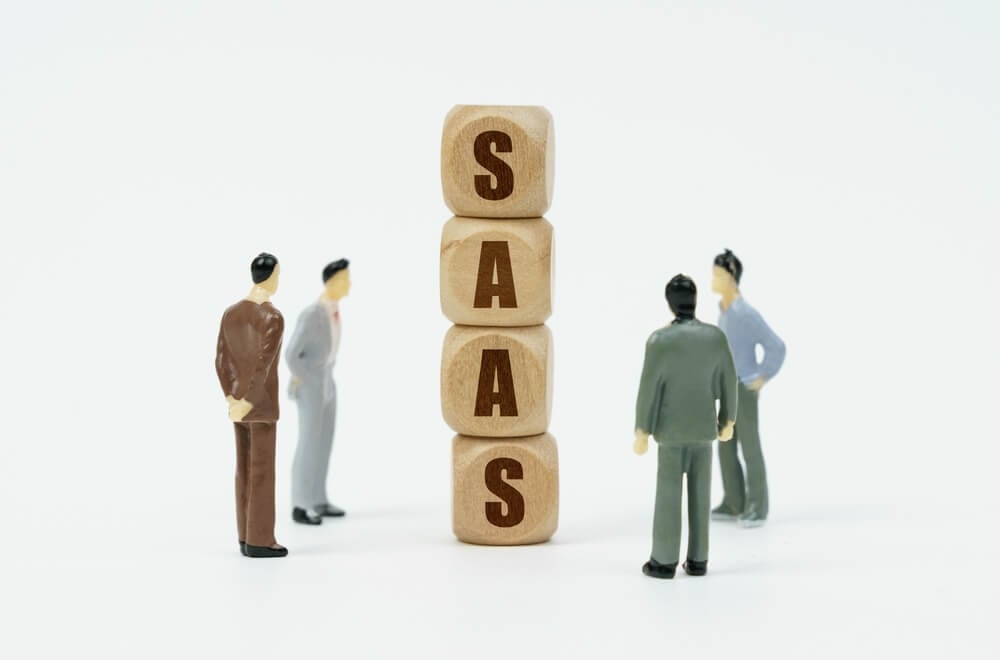 SaaS SEO_Technology and business concept. On a white background, figures of businessmen look at wooden cubes with the inscription - SAAS