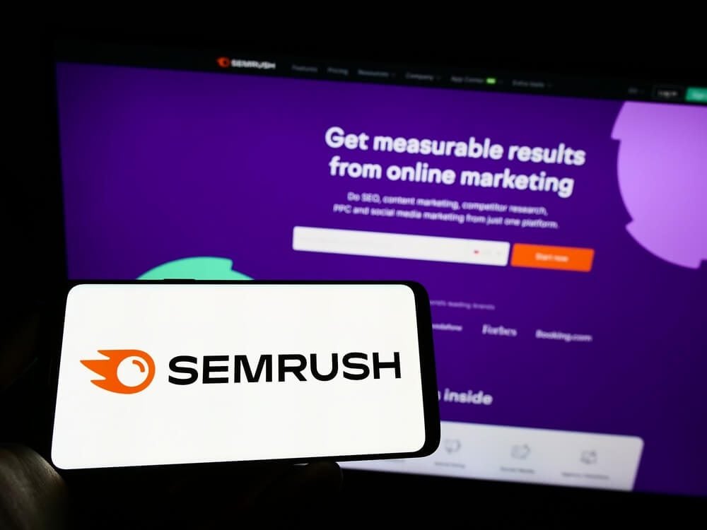 SEMrush_Stuttgart, Germany - 09-25-2022: Person holding mobile phone with logo of US search engine marketing company SEMrush Inc. on screen in front of web page. Focus on phone display. Unmodified photo.
