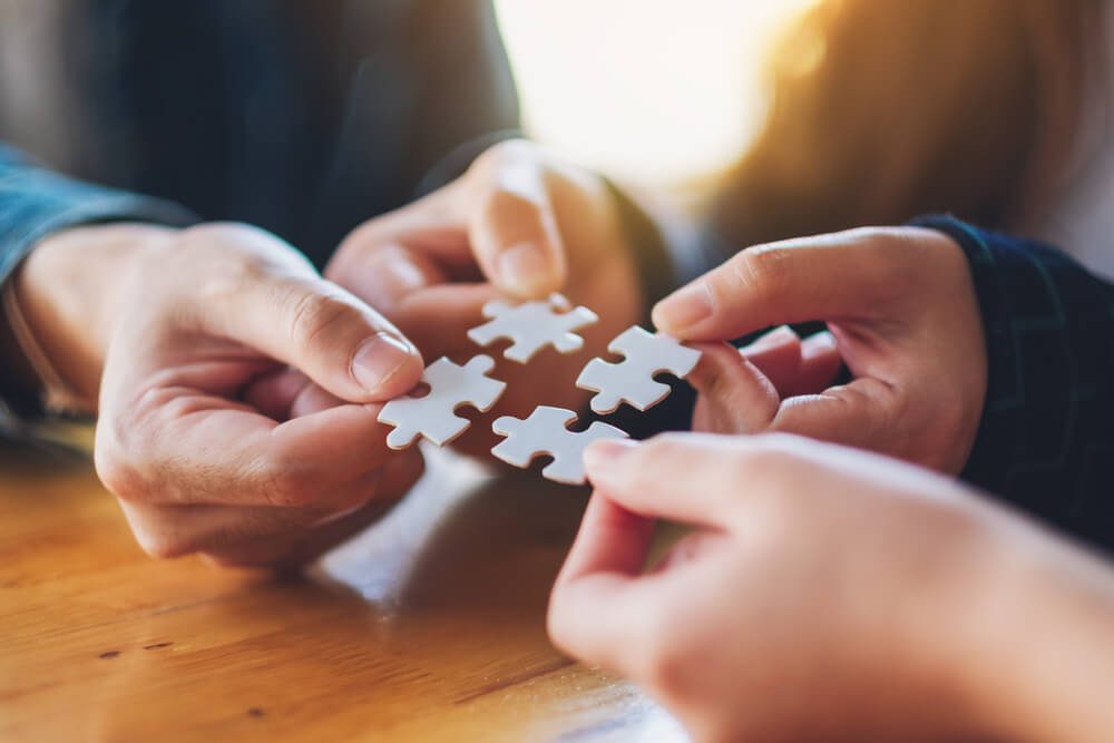 link building_Closeup image of a group of people holding and putting a piece of white jigsaw puzzle together