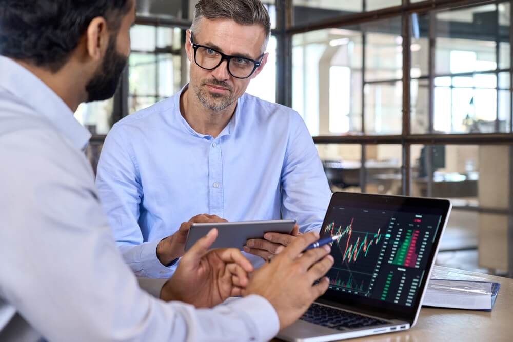 website indexing_Diverse managers traders analysts discussing financial growth market at desk with laptop with graphs on screen using tablet device. Investors brokers analysing indexes online cryptocurrency stock.