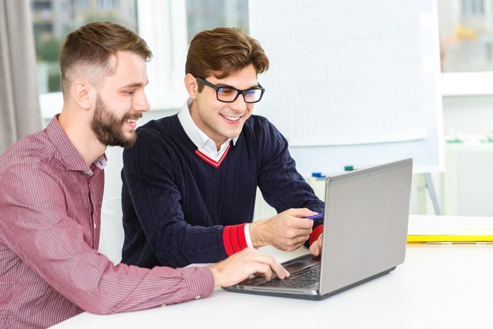 seo professional_Discussing project. Shot of two male co-workers working together on a laptop smiling cheerfully