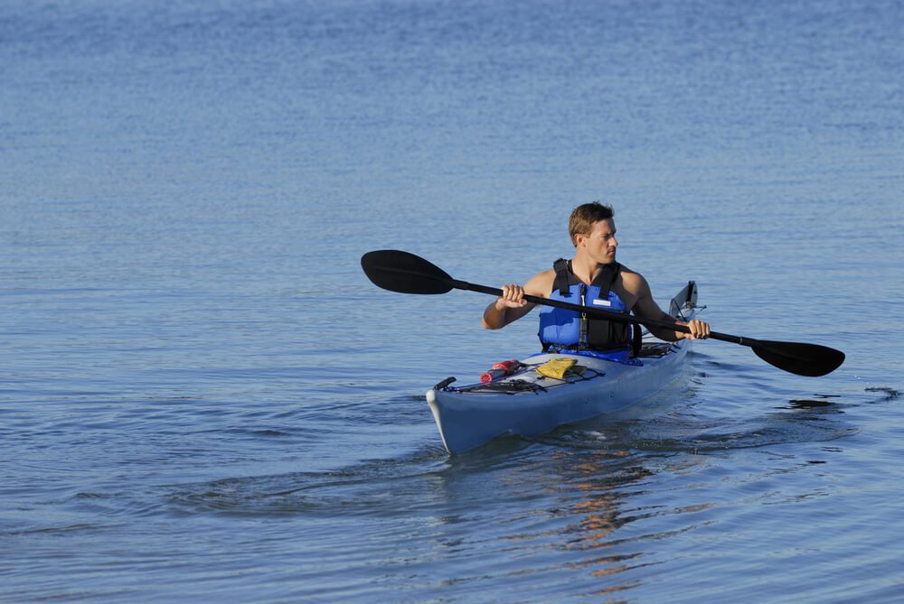 San Diego Kayak_An athletic man is backing off the shore into calm blue waters of Mission Bay, San Diego, California. Copy space on top and left.