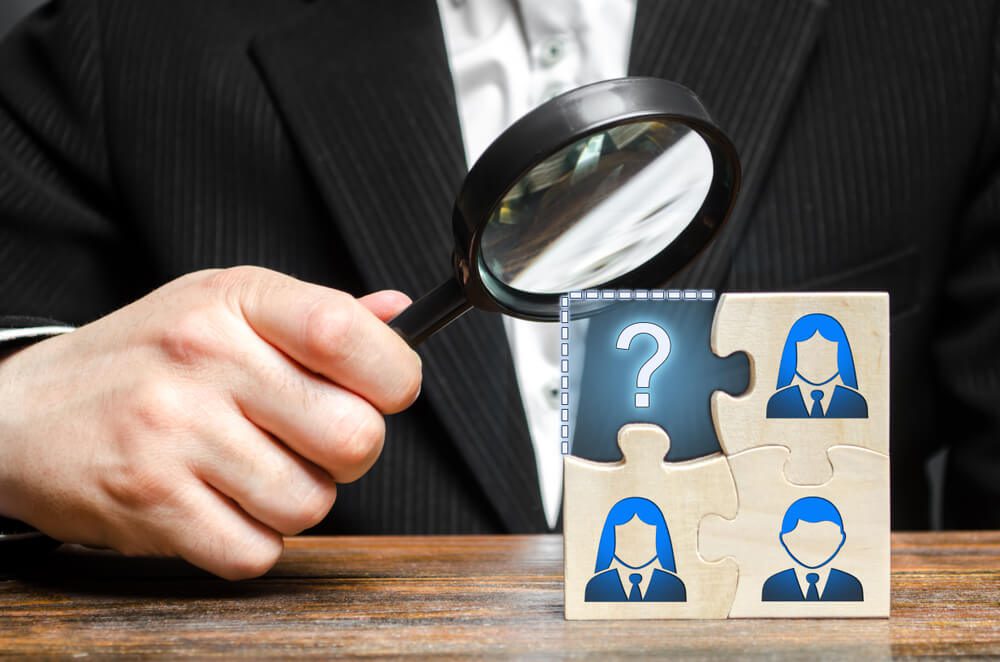 hire marketing_Businessman with a magnifying glass examines the missing part of the puzzle team. Search, recruitment staff, hiring leader. Creating an effective business team. Lack of specialists in the labor market
