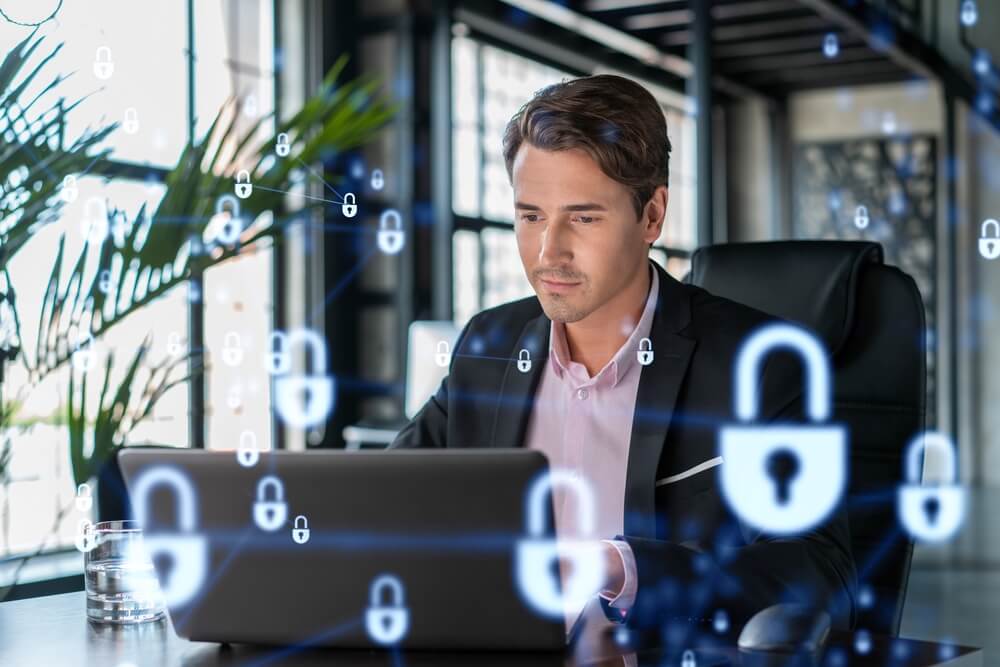 click fraud_Handsome businessman in suit at workplace working with laptop to defend customer cyber security. Concept of clients information protection and brainstorm. Padlock hologram over office background.