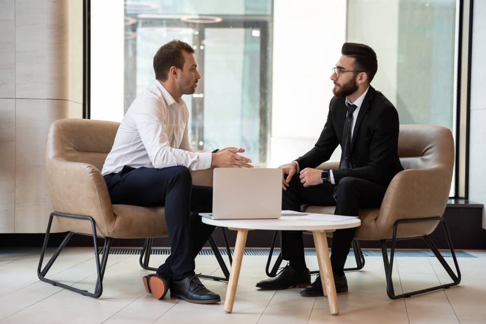 consultant_Serious multiethnic male business partners talk discussing potential cooperation or shared project, concentrated successful international businessmen speak brainstorm at meeting or briefing in office