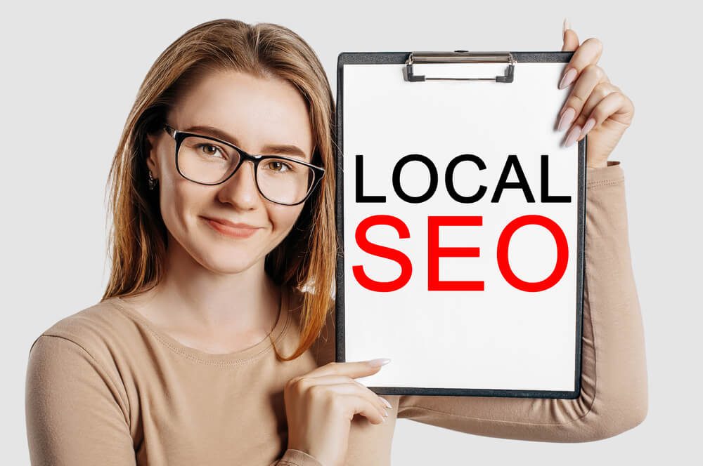 local seo_LOCAL SEO. Beautiful young business woman wearing glasses holds a clipboard with mock up space isolated on gray background