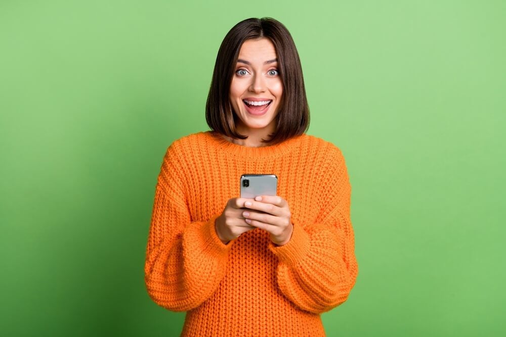 mobile app trends_Portrait of attractive cheerful amazed girl using gadget social network post isolated over bright green color background