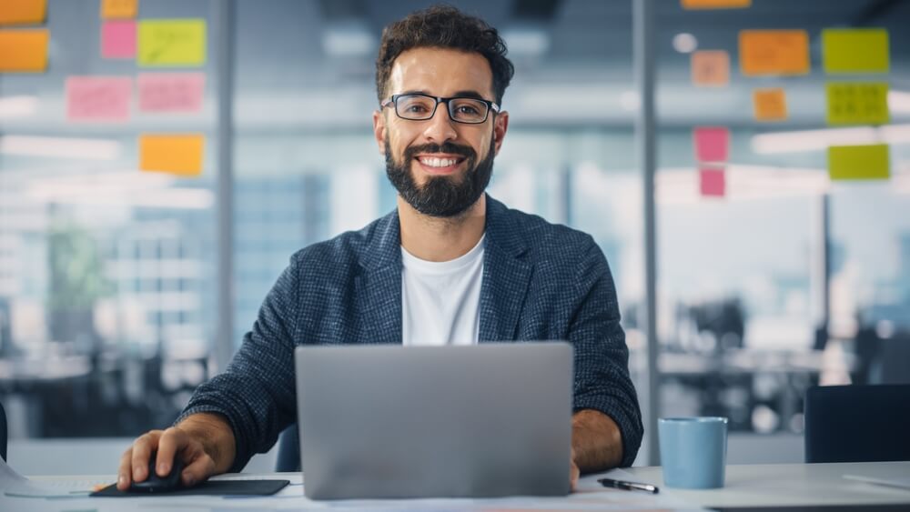 digital marketing_Modern Office: Portrait of Stylish Hispanic Businessman Works on Laptop, Does Data Analysis and Creative Designer, Looks at Camera and Smiles. Digital Entrepreneur Works on e-Commerce Startup