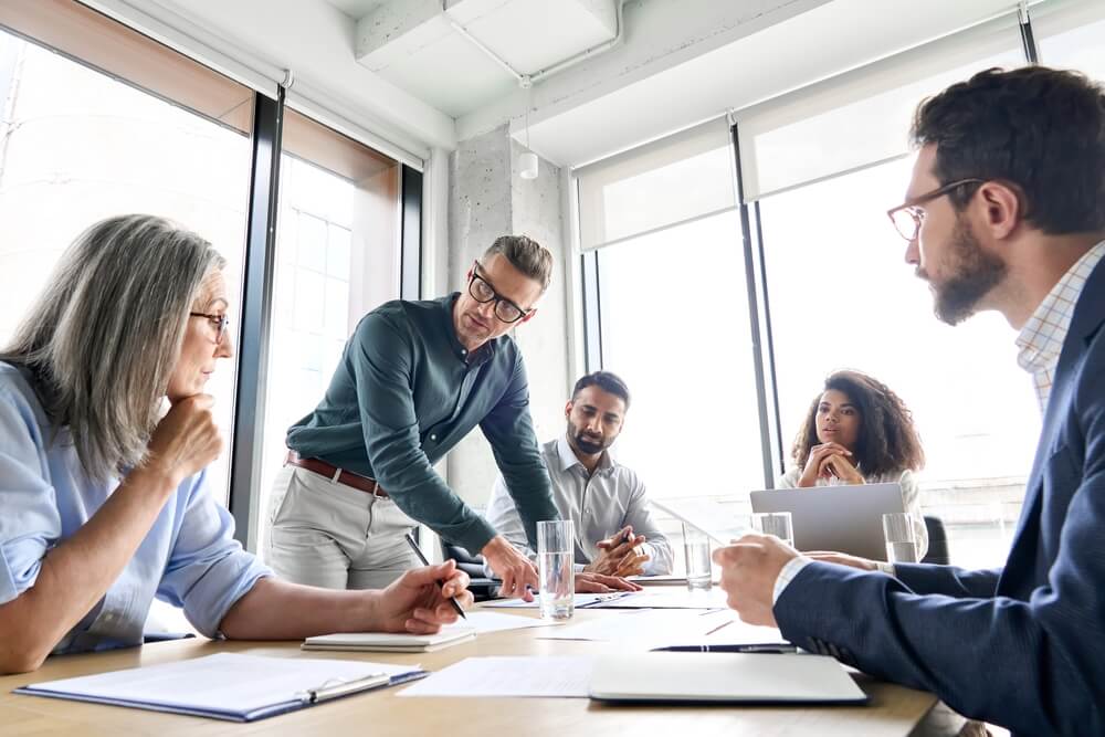 consultant_Male mature caucasian ceo businessman leader with diverse coworkers team, executive managers group at meeting. Multicultural professional businesspeople working together on research plan in boardroom.