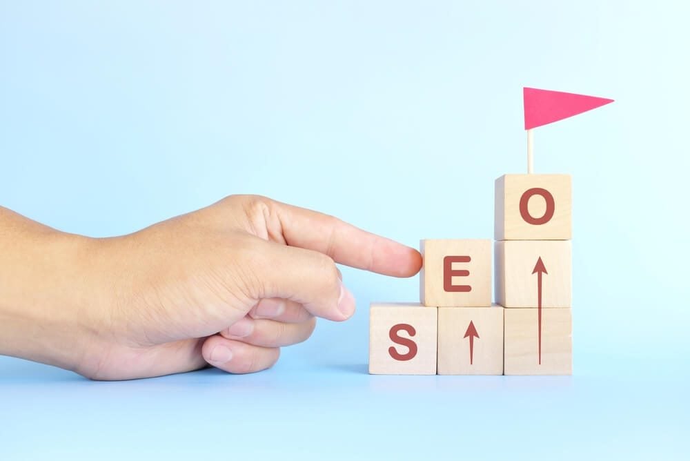 seo ranking_Business SEO or search engine optimization ladder to success concept. Human hand climbing wooden blocks with red flag.