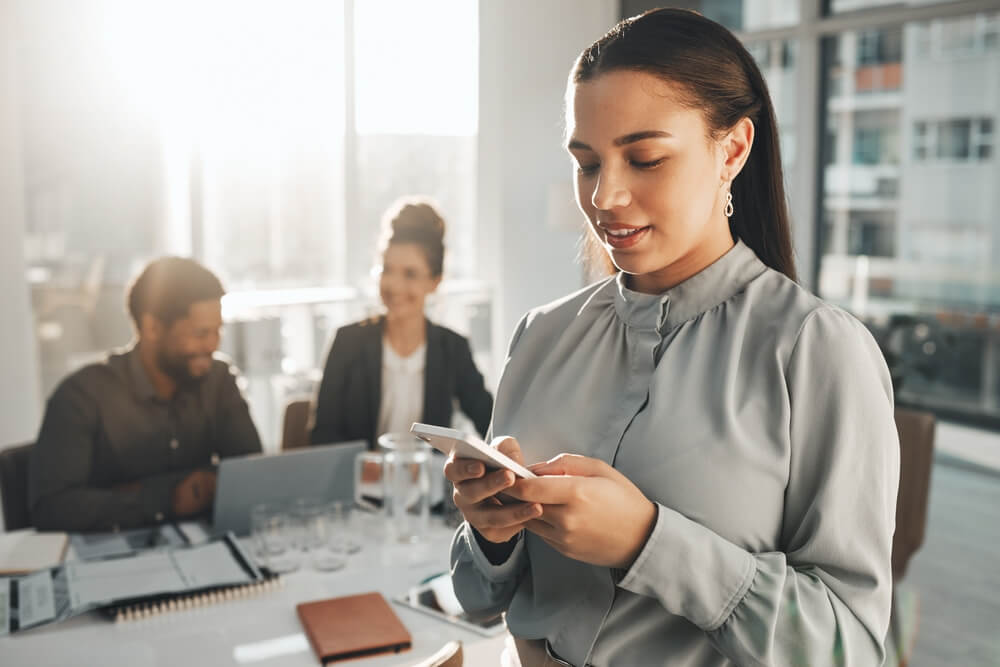 mobile app_Business woman, phone text and teamwork meeting with a female employee on a mobile app. Office, corporate team and online chat of a financial analytics worker on a cellphone reading website content