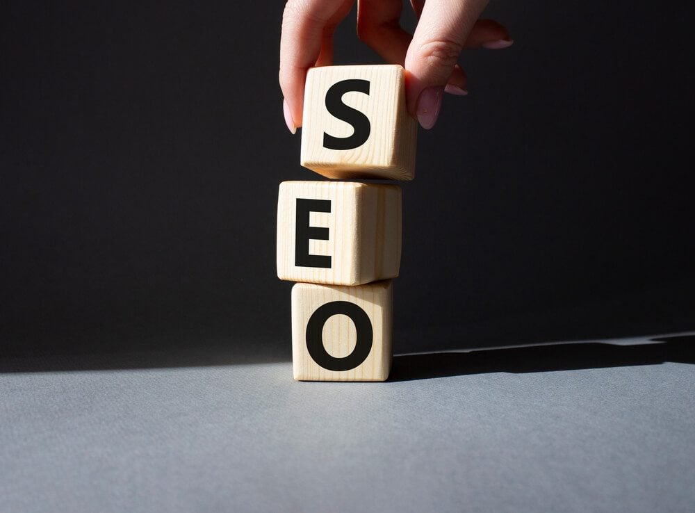 SEO_SEO - Search Engine Optimization symbol. Wooden blocks with words SEO. Businessman hand. Beautiful grey background. Business and SEO concept. Copy space