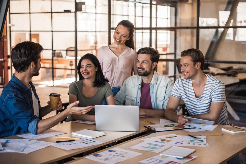 marketing strategy_Beautiful young business people in casual clothes are using a laptop, talking and smiling while working in office