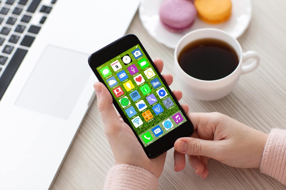 app store_woman hands holding white phone with home screen icons apps near notebook