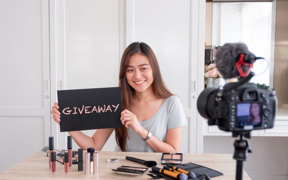business giveaways_Asian young female blogger giveaway gift to fan following channel while recording vlog video with makeup cosmetic at home online influencer on social media concept.live streaming viral
