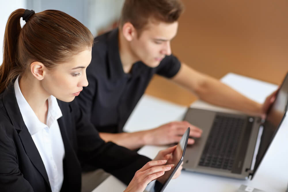 digital partner_Two beautiful young businesspeople sitting at table in office and working at laptop and tablet pc