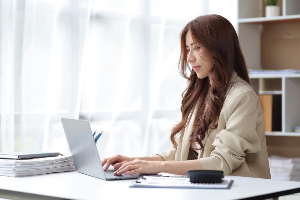 marketing officer_Business woman in office working with laptop and financial documents on desk.