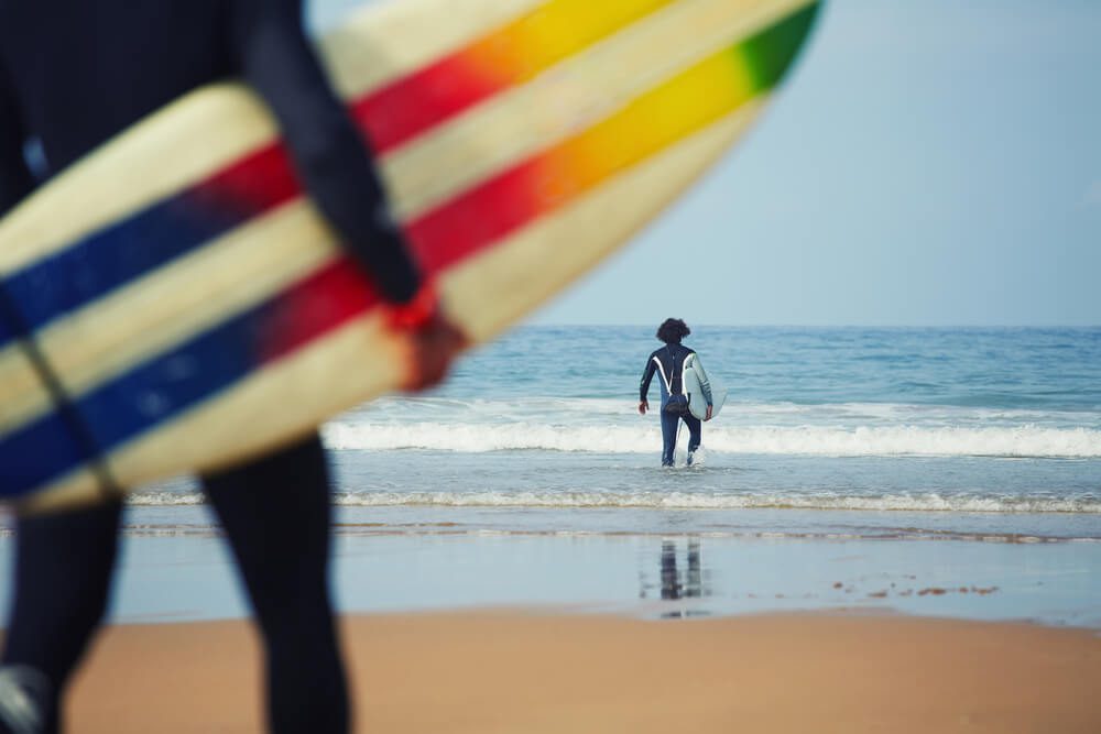 surfing school_Professional surfers carrying their surfboards while going to the sea, professional surfers in black diving suits ready to surf walk to the ocean, close up of surfboard with surfer on background