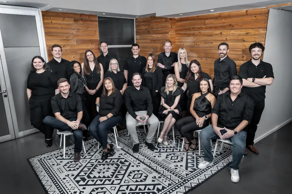 Large group of colleagues dressed in black posing together for a team photo in an office.
