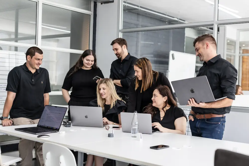 Group of colleagues collaborating around a table with laptops during a team meeting in an office.