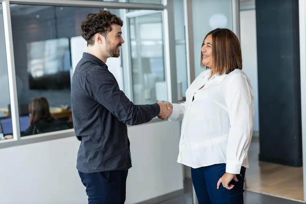Two colleagues smiling and shaking hands in an office setting.