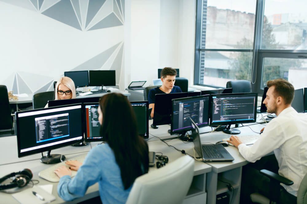 custom software development_People Working In Modern Office. Group Of Young Programmers Sitting At Desks Working On Computers In It Office. Team At Work. High Quality Image