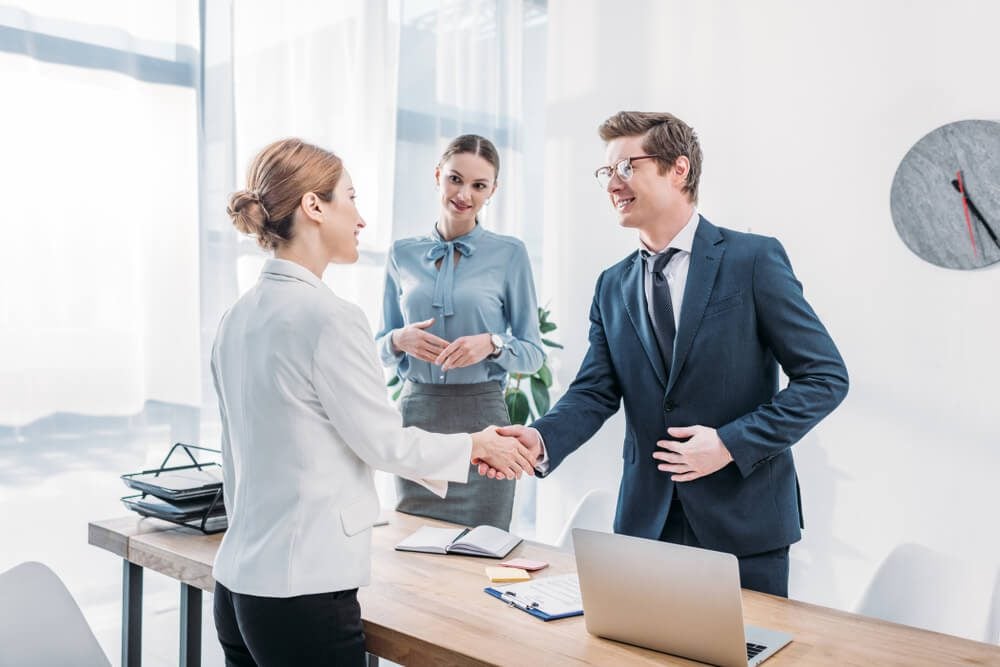 marketing agency_cheerful recruiter shaking hands with woman near colleague in office