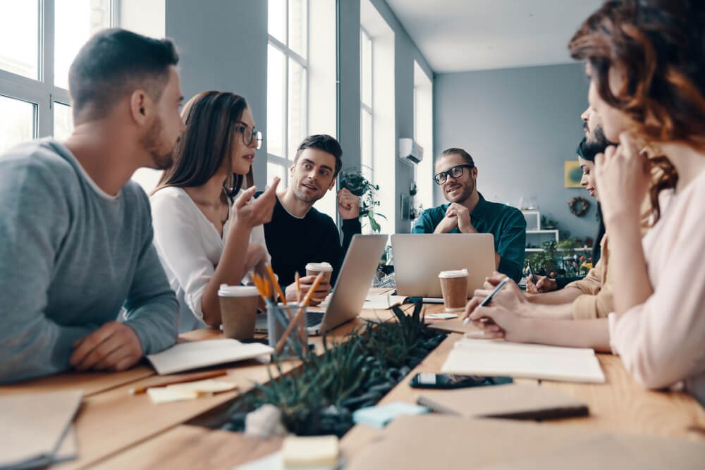 marketing strategy_Determined to be the best. Group of young modern people in smart casual wear discussing something and smiling while working in the creative office