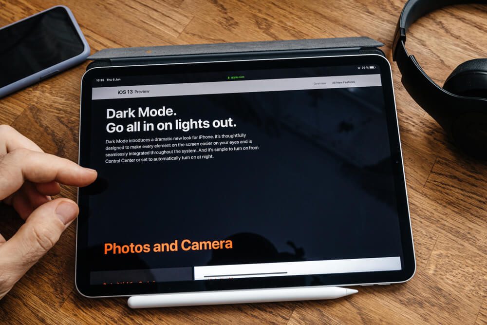 dark mode_Paris, France - Jun 6, 2019: Man reading on Apple iPad Pro tablet about latest announcement of at Apple Worldwide Developers Conference (WWDC) - showing the new Dark Mode on iOS iPhone