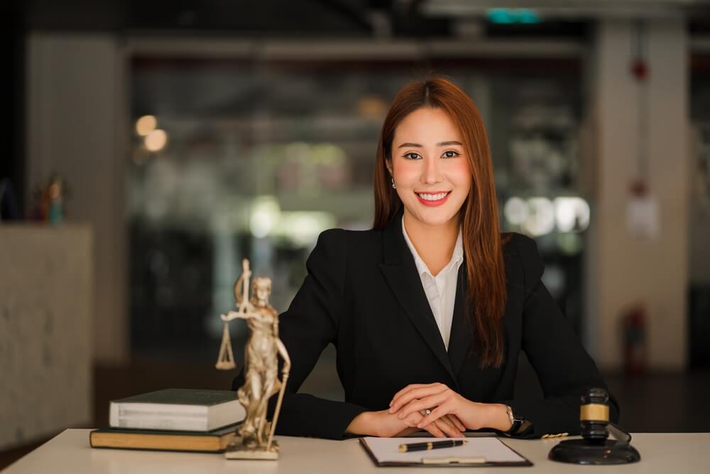 lawyer_Attractive Asian Lawyer Female Lawyer Discussing Contract Documents with Golden Goddess Scales with Hammer on Wooden Tables in Office of Legal Services, Advice, Justice and Real Estate Ideas.