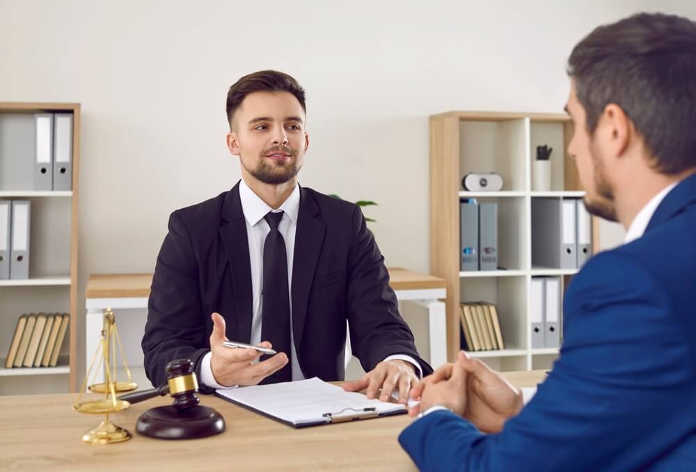 lawyer_Lawyer having a meeting with a new client. Young male attorney in suit and tie sitting at office desk, sharing legal advice, explaining inheritance process, trying to help. Law consultation concept