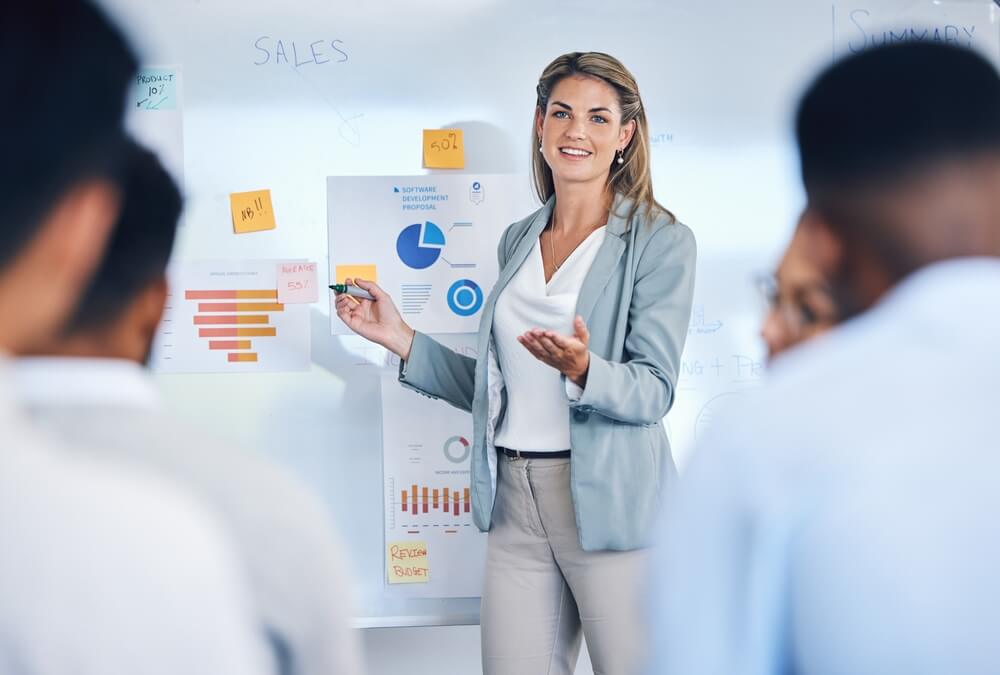 b2b analytics_Sales, marketing and b2b strategy of business woman speaker giving a presentation to work crowd. Corporate advertising seminar with female present sale analytics and logistics chart on white board