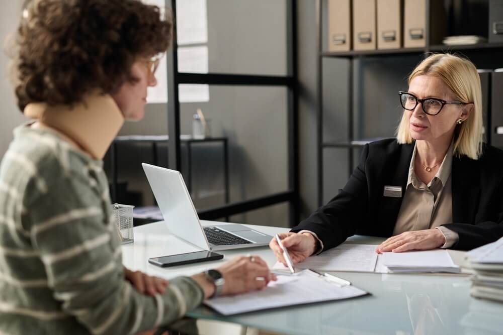 personal injury law_Portrait of female insurance broker consulting injured young woman in office after accident and pointing at legal forms