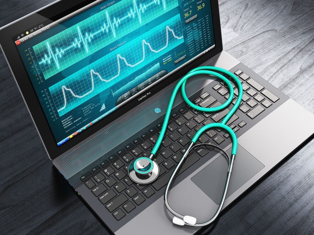 healthcare custom software_Healthcare, medicine and cardiology tool concept: laptop or notebook computer PC with medical cardiologic diagnostic test software on screen and stethoscope on black wooden business office table
