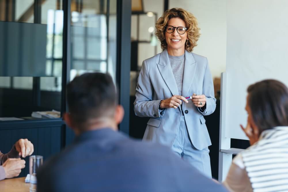 lead demand_Mature business woman having a discussion with her team. Woman leading a meeting in an office. Business woman presenting her ideas in an office. Group of professionals planning a project.