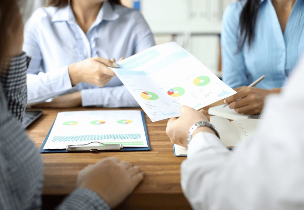 demand generation_Close-up of male hand giving documents with diagram and graph to woman in blue blouse. Biz team discussing statistics report. Business and teamwork concept.