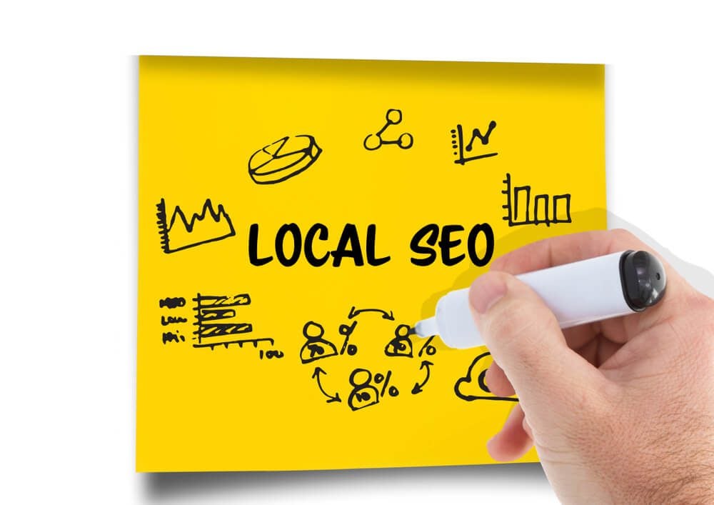 local SEO_Digital composite of Local Seo graphic on a post-it. Hand with pen drawing it.
