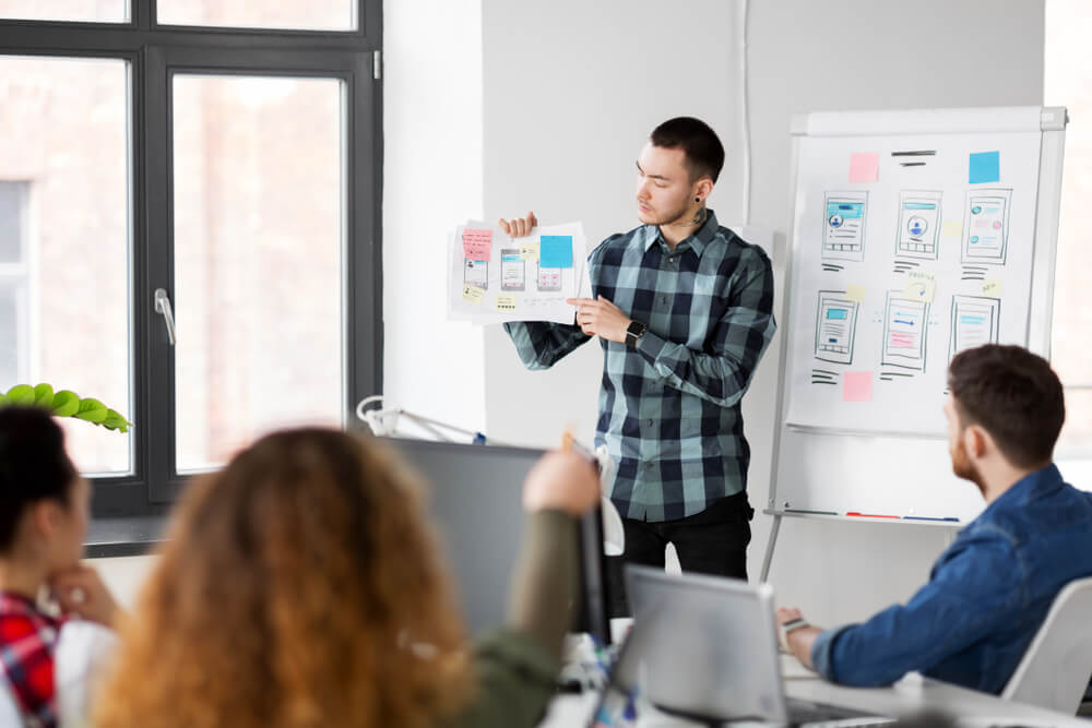 user experience UX_business, technology and people concept - man showing user interface design on flip chart to creative team at office presentation