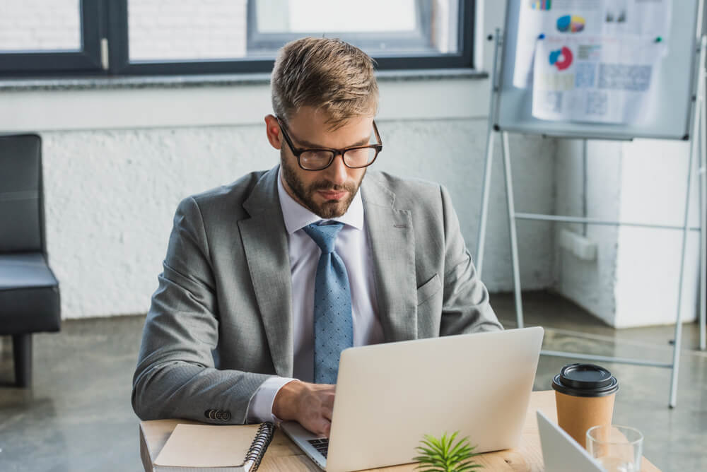 lead and demand_focused young businessman in suit and eyeglasses using laptop at workplace