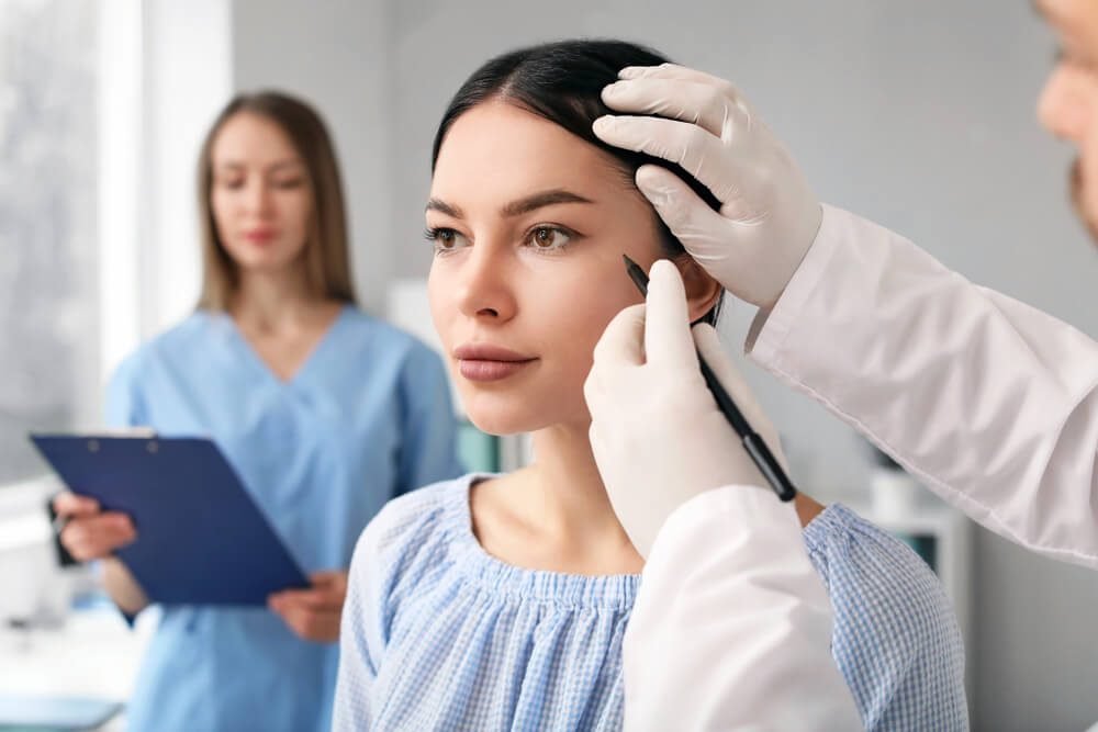 plastic surgeon_Plastic surgeon applying marks on patient's face in clinic