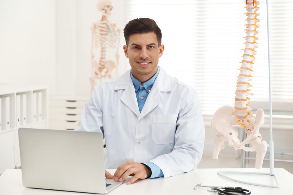 chiropractic seo_Male orthopedist with laptop near human spine model in office