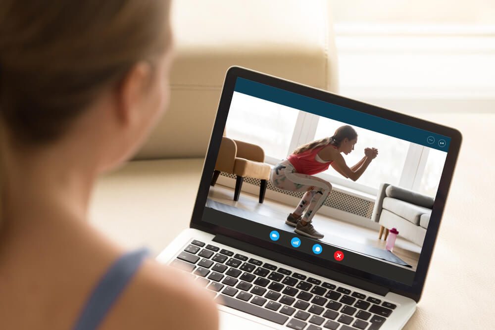 personal trainer_Focus on laptop screen with young woman in sportswear doing morning exercises, deep squats on yoga mat, staying fit at home. Interested girl watching online educational fitness workshop training.