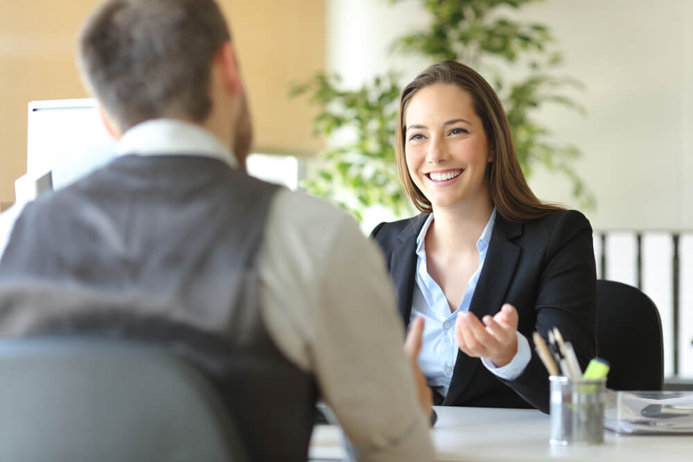 CMO hire_Happy executive coworkers laughing and talking sitting on a desk at the office